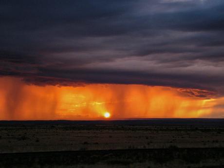 A dramatic sunset with dark clouds and an orange glow in the sky, creating a stunning silhouette of the landscape below.