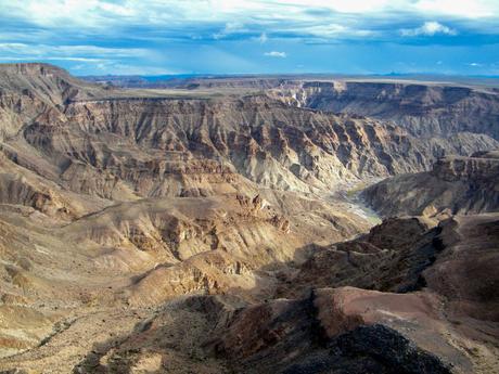 A wide view of the Fish River Canyon in Namibia, showcasing rugged cliffs and deep, winding valleys under a partly cloudy sky.