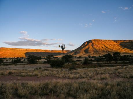 A sunset landscape in Namibia with an isolated windmill silhouetted against the golden light reflecting off distant hills.