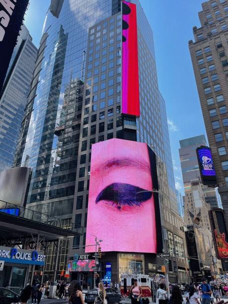 A massive digital billboard displaying a close-up of an eye against a backdrop of mirrored skyscrapers in Times Square.