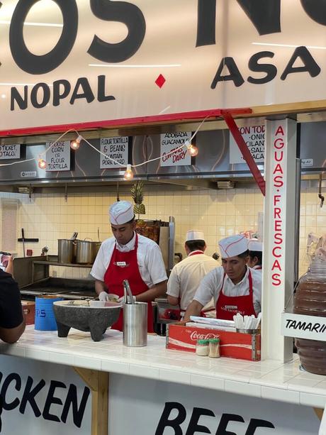 Staff working at a taco stand inside Los Tacos No. 1, preparing fresh food for customers.