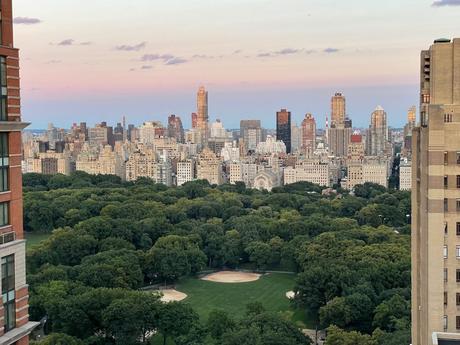 A view of Central Park’s treetops, looking toward the New York City skyline at dusk, with buildings glowing in the fading light.