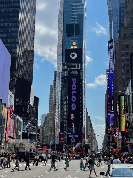 A view of Times Square with tall buildings and a large billboard featuring rapper Polo G promoting his album 'Hood Poet.'