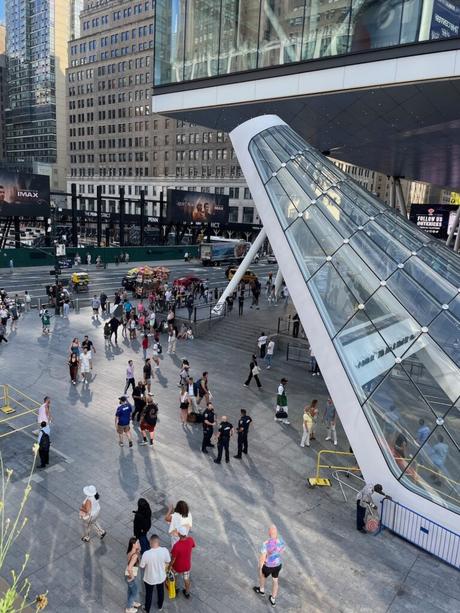 An elevated view of people walking around the plaza in front of the entrance to the Moynihan Train Hall in New York City.