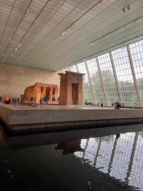 The Temple of Dendur exhibit inside the Metropolitan Museum of Art, featuring the ancient sandstone structure displayed against a large window with a reflecting pool in the foreground.