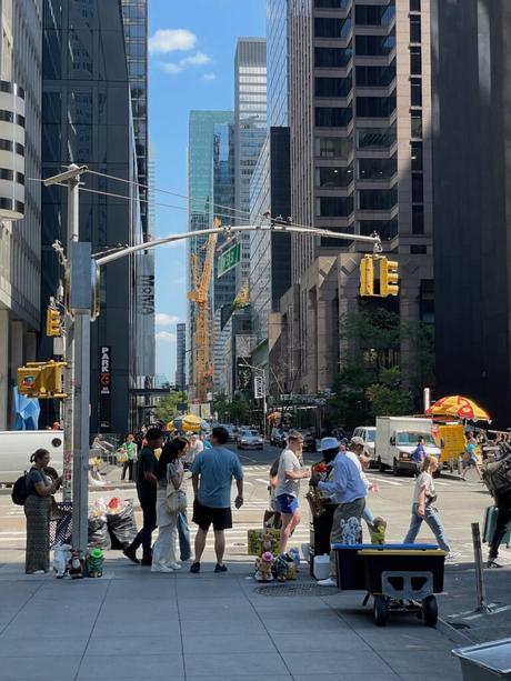 A bustling Manhattan street with skyscrapers in the background, street vendors, and pedestrians walking around.