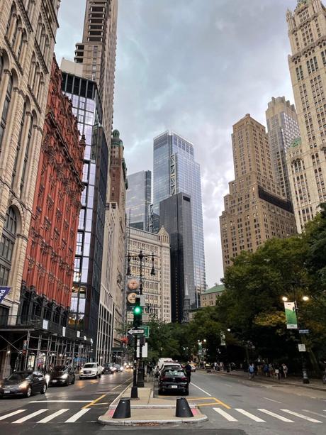 A view of Woolworth Building and other historic and modern skyscrapers in downtown Manhattan, with cars and people bustling on the streets below.