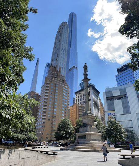 Columbus Circle in New York City, with the Christopher Columbus monument in the foreground and tall modern skyscrapers in the background.