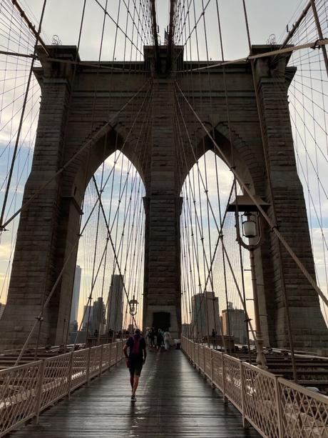 A close-up of one of the large stone towers of the Brooklyn Bridge, with its iconic suspension cables spreading out against the sky.