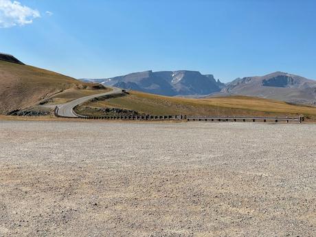 A winding road leading through a barren, rocky landscape with distant mountains, captured under a bright blue sky.