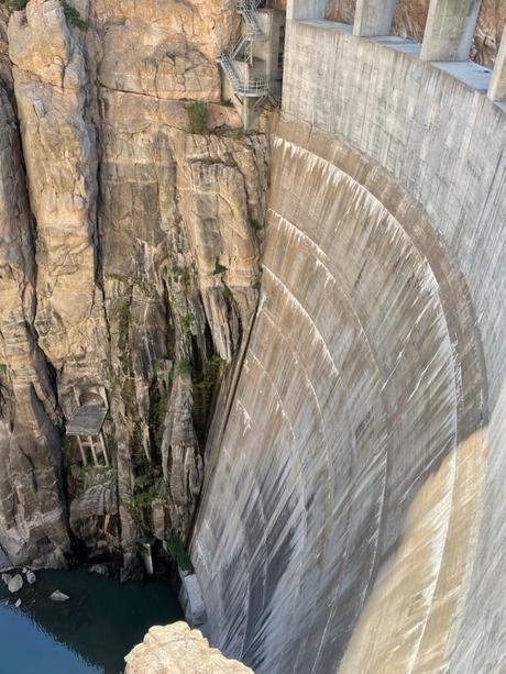 A large concrete dam called Buffalo Bill Dam built into a rocky cliff face near Cody, Wyoming, with steep drops and metal staircases visible on the structure.