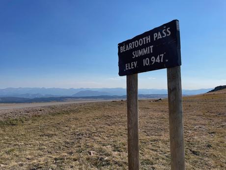 A wooden sign marking the summit of Beartooth Pass at an elevation of 10,947 feet, with mountain ranges visible in the background.