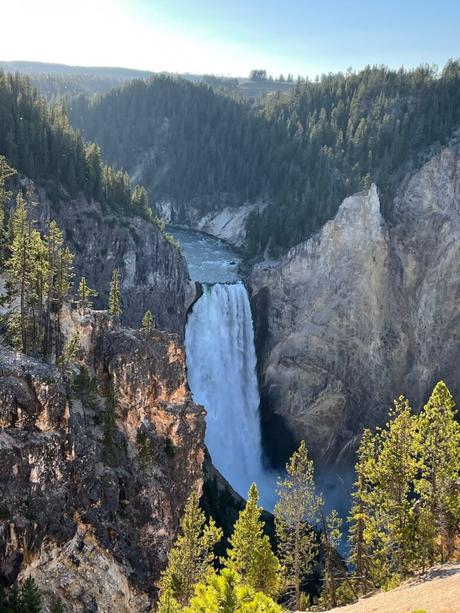 A large waterfall cascading into a deep canyon, surrounded by cliffs and dense forest, with mist rising from the base of the falls.