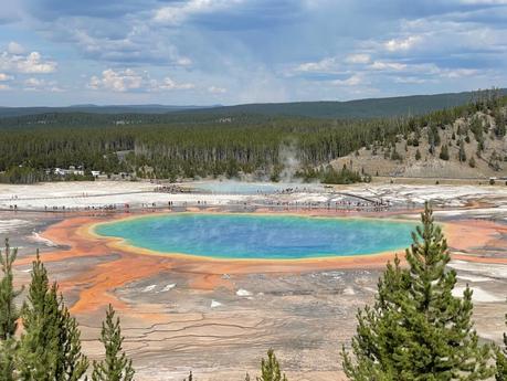 A stunning view of the Grand Prismatic Spring in Yellowstone National Park, with vibrant blue, orange, and green hues surrounded by a crowd of visitors.