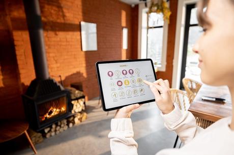 Woman using smart device to control home heating in front of fireplace and brick wall