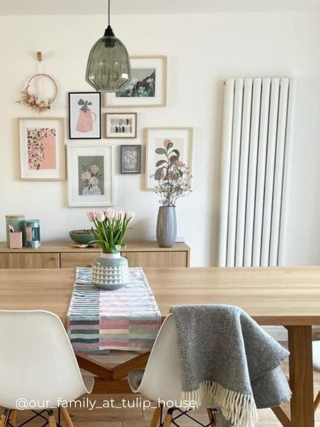 a white vertical radiator on a white wall next to multiple framed pictures in a dining room