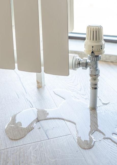 a leaky white designer radiator with water on the floow under the valve