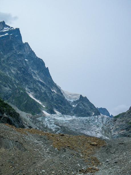 A close-up of a glacier cascading down the mountainside, its blue-tinted ice contrasting starkly with the dark, craggy rocks that frame the scene.