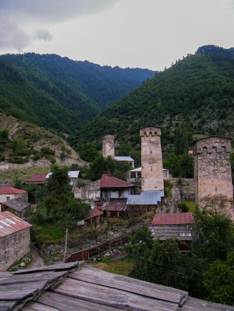 Three medieval stone towers rise from the center of a small village, their weathered facades standing in stark contrast to the dense, green hills that encircle them.