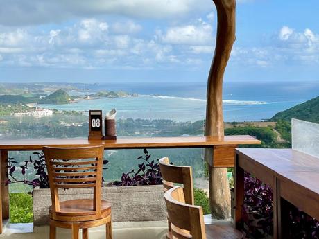 A restaurant table overlooking a breathtaking view of a coastline with rolling hills and the blue ocean in the distance.