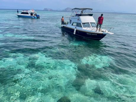 A pair of motorboats with people standing on the deck in the shallow turquoise waters of the Komodo Islands.