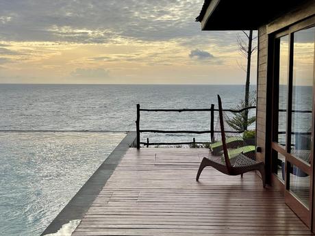 A peaceful scene showing an infinity pool merging with the ocean horizon at sunset, with soft orange and pink hues reflecting in the pool.