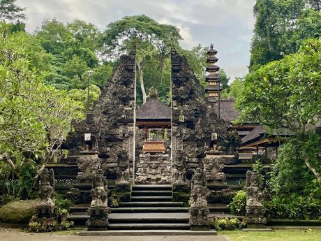 Ornate Balinese temple entrance, featuring detailed stone carvings surrounded by greenery, trees, and a serene setting.