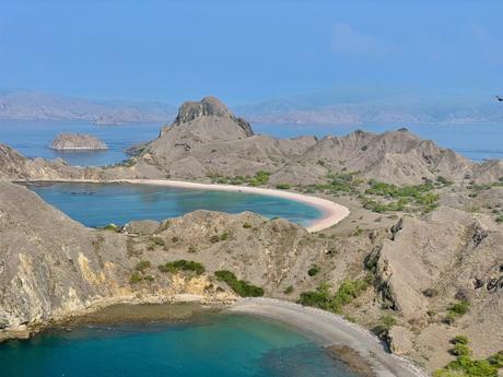 An aerial view of the sweeping, arid landscape of Padar Island, Indonesia, with its famous curved beaches and turquoise waters nestled between rugged hills.