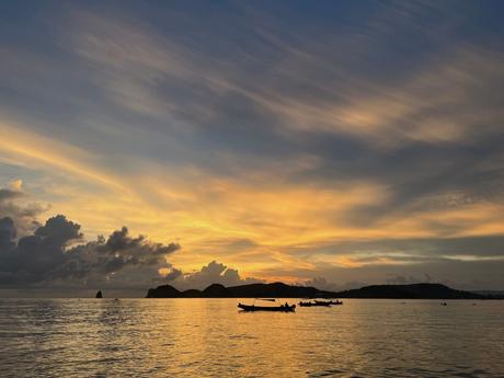 A vibrant sunset over the ocean, with the sky painted in shades of orange and purple, and boats silhouetted against the horizon.