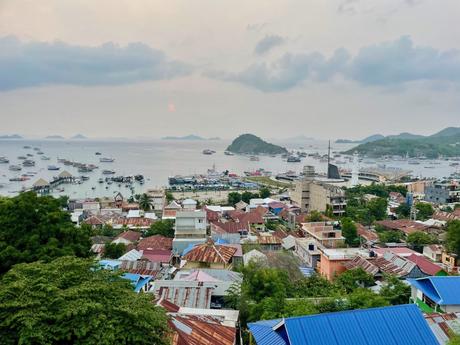 Overlooking a busy harbor in Labuan Bajo, Indonesia, with boats docked and colorful rooftops of buildings in the foreground.