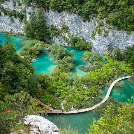 An aerial view of Plitvice Lakes National Park in Croatia, with vibrant turquoise waters and lush greenery surrounding a wooden footbridge.