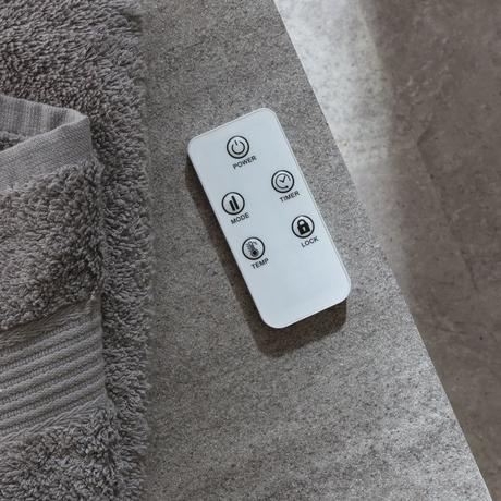 ECOSO white smart electric heated towel rail with fan remote on settee next to gray towel