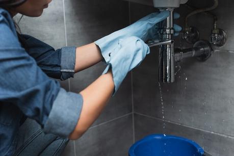 Woman with blue rubber gloves repairing pipe with spanner