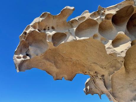 A close-up of a uniquely shaped rock formation with natural holes and curves, set against a bright blue sky.