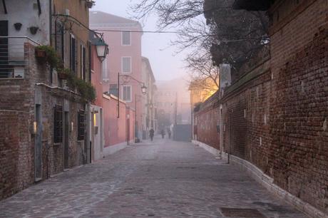 A quiet, misty Venetian alley lined with brick buildings, street lamps glowing softly in the distance.