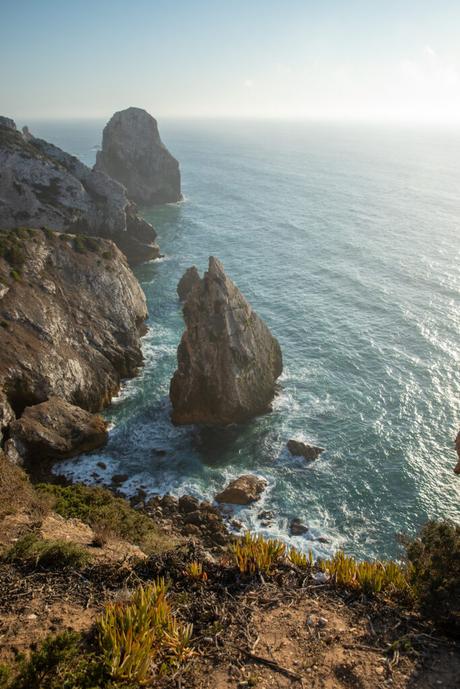 A breathtaking cliffside view with jagged rock formations jutting out into the ocean. The waves crash against the steep cliffs below, and a few patches of greenery dot the rocky landscape.