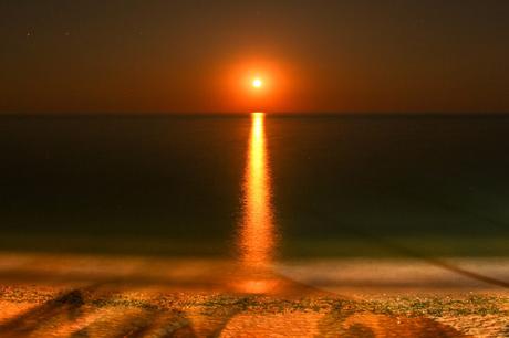 A breathtaking view of the sun rising over the Black Sea, its warm light reflected on the calm water. The sky is dark orange and fades into deep blue.