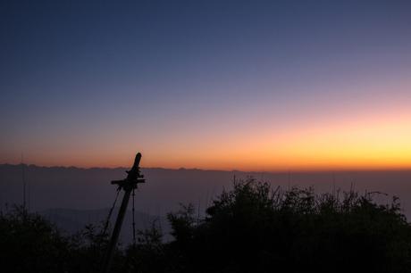 A vibrant sunrise or sunset over distant mountains, with a silhouette of a wooden post in the foreground.