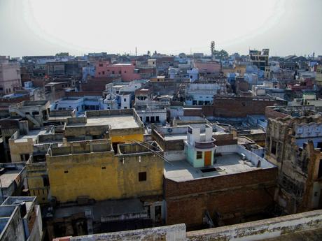 A cityscape with tightly packed buildings, mostly flat rooftops, painted in shades of yellow, brown, and gray.