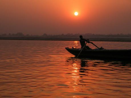 A silhouette of a man rowing a boat at sunset, with the sun casting an orange glow across the calm waters.