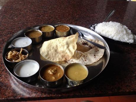 A South Indian thali served on a metal tray with various curries, chutneys, rice, chapati, and papadum.