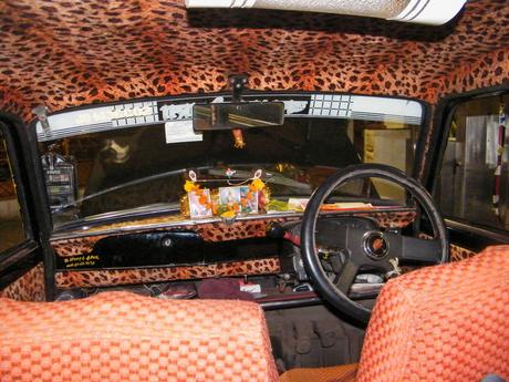 The interior of a taxi with leopard-print seat covers and a dashboard adorned with small pictures and religious symbols.