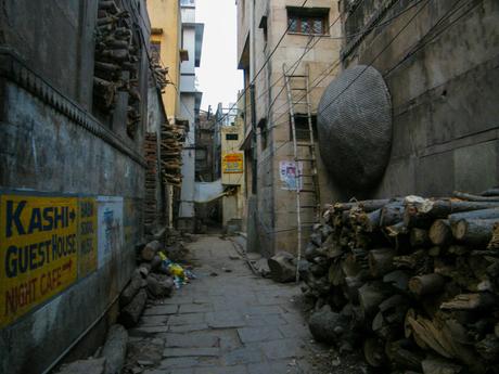 A dimly lit alley with stacks of firewood lining the walls and a guesthouse sign directing towards a night cafe.