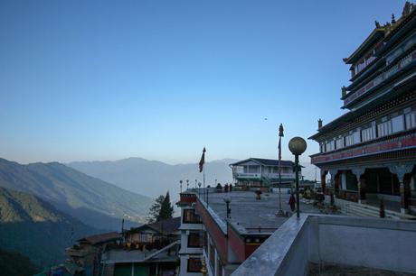 A monastery perched on a mountain with breathtaking views of distant hills and a clear blue sky.