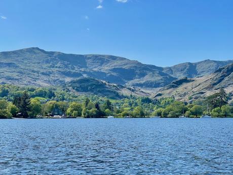 A calm lake reflecting the rugged mountains in the distance. The bright blue sky enhances the natural beauty of the scene.