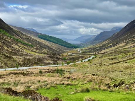 A wide glacial valley in the Northwest Highlands with a road running along the bottom and cloudy skies above.