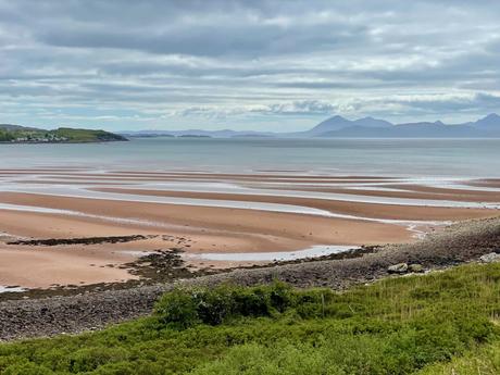 A view of a terracotta coloured beach partially covered by the sea near Applecross with the mountains of the Isle of Skye visible in the distance across the sea.