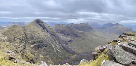 A panoramic view of the vast Torridon mountain range, with multiple jagged peaks under a cloudy sky, showcasing the rugged beauty of the terrain.