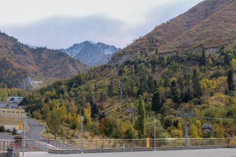 A view of a cable car line stretching up the wooded mountainside with snow-capped peaks in the background, taken in Medeu, Kazakhstan.