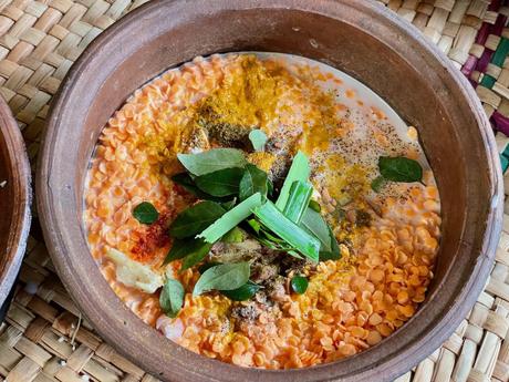 A clay pot filled with red lentils, spices, coconut milk, and fresh herbs, ready to be cooked. The ingredients are colorful, representing traditional Sri Lankan cuisine.